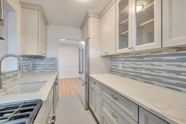 kitchen featuring light stone countertops, sink, backsplash, high end fridge, and light tile patterned floors