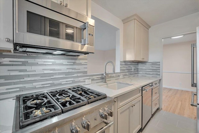 kitchen featuring backsplash, sink, light wood-type flooring, appliances with stainless steel finishes, and light stone counters