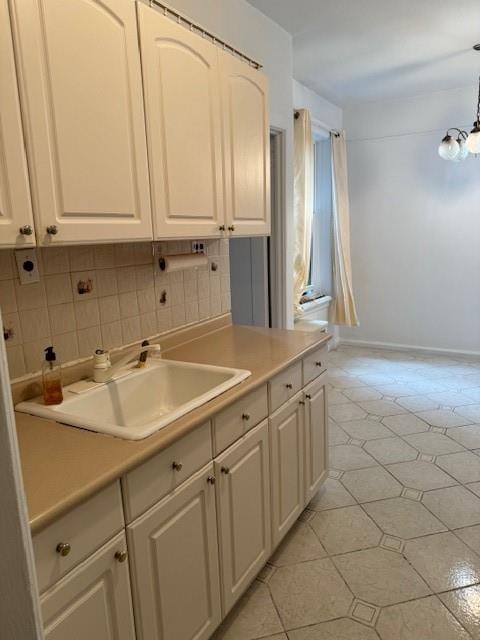 kitchen featuring sink, backsplash, a chandelier, pendant lighting, and light tile patterned floors