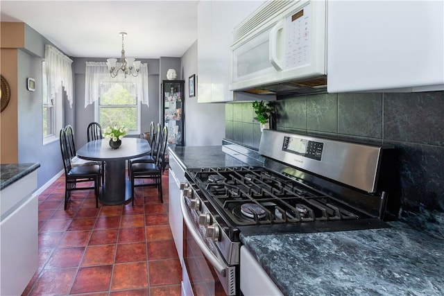 kitchen featuring backsplash, an inviting chandelier, dark tile patterned flooring, gas stove, and white cabinetry