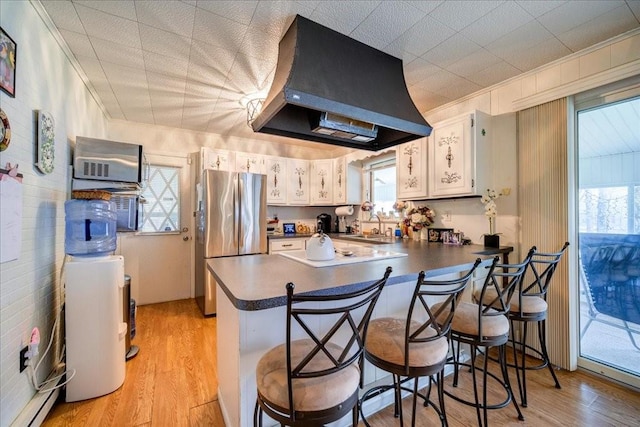 kitchen featuring white cabinets, ventilation hood, light hardwood / wood-style flooring, stainless steel fridge, and kitchen peninsula