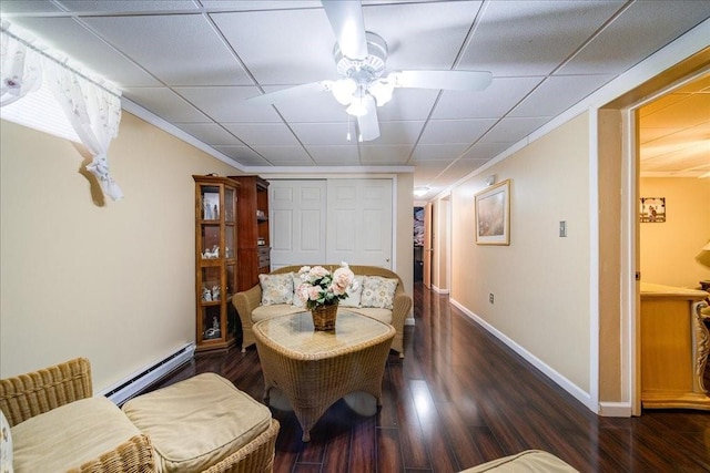 dining area with a drop ceiling, baseboard heating, crown molding, dark wood-type flooring, and ceiling fan