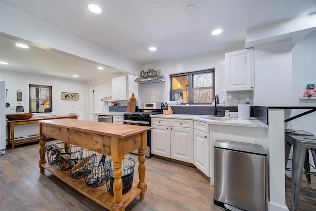 kitchen with stainless steel gas range oven, backsplash, sink, light hardwood / wood-style flooring, and white cabinetry