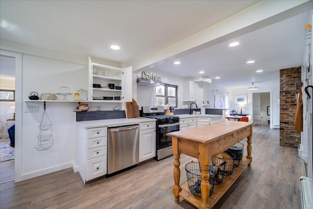 kitchen featuring white cabinetry, sink, stainless steel appliances, kitchen peninsula, and hardwood / wood-style flooring