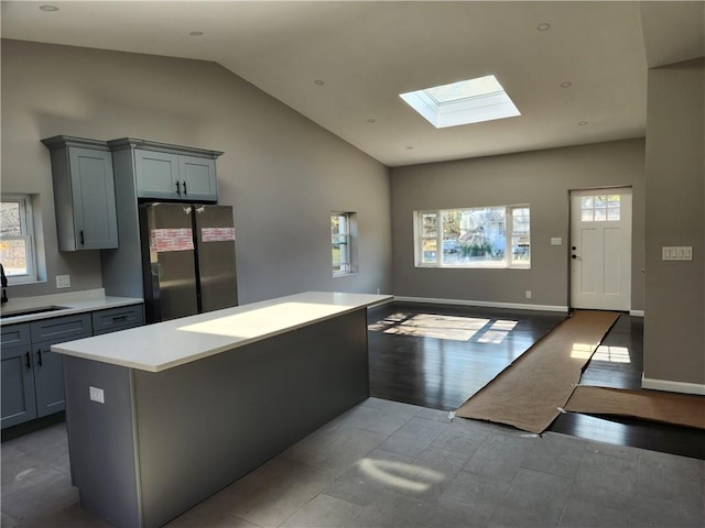 kitchen with stainless steel fridge, gray cabinets, light hardwood / wood-style floors, and lofted ceiling with skylight