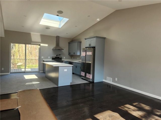 kitchen with a skylight, wall chimney range hood, gray cabinets, a kitchen island, and appliances with stainless steel finishes