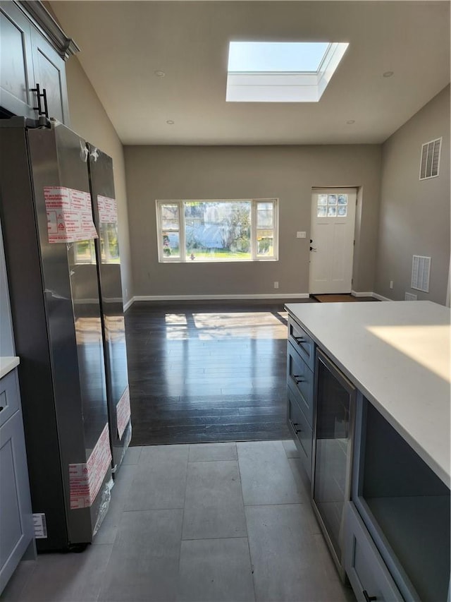 kitchen featuring wine cooler, stainless steel fridge, vaulted ceiling with skylight, and light hardwood / wood-style floors