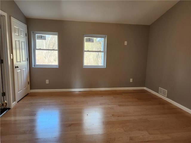 empty room featuring light wood-type flooring, vaulted ceiling, and a healthy amount of sunlight