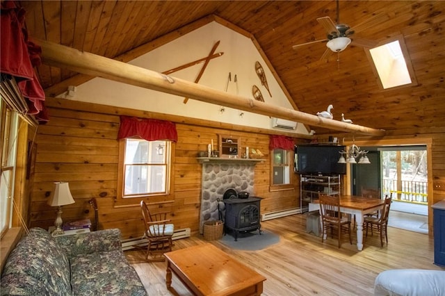 living room with a wood stove, a baseboard heating unit, wooden walls, a skylight, and light wood-type flooring