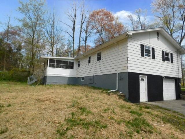 view of home's exterior with a sunroom, a garage, and a lawn