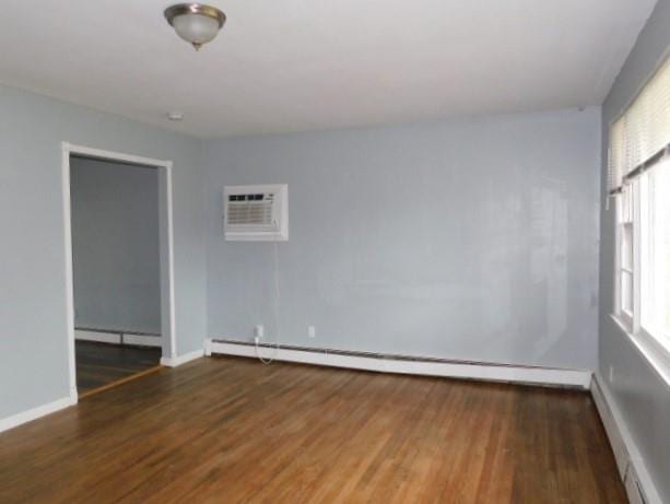 unfurnished room featuring a wall mounted air conditioner, dark hardwood / wood-style floors, and a baseboard heating unit