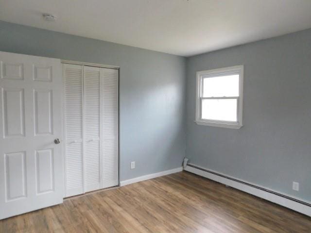 unfurnished bedroom with hardwood / wood-style floors, a baseboard radiator, and a closet