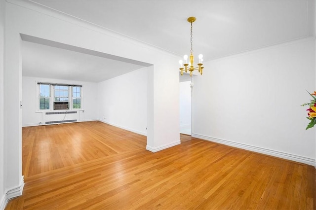 spare room with crown molding, a notable chandelier, light wood finished floors, radiator heating unit, and baseboards