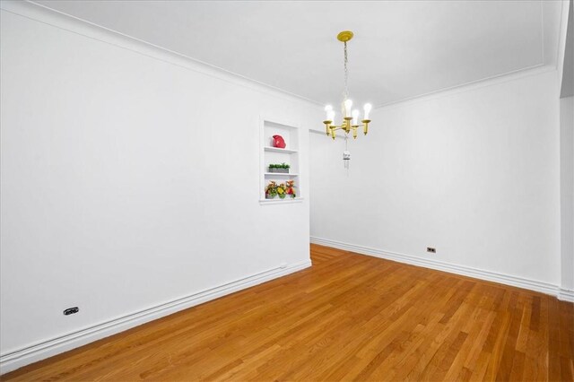 spare room with light wood finished floors, baseboards, built in features, crown molding, and a notable chandelier