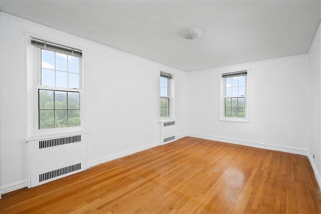 unfurnished room with baseboards, hardwood / wood-style flooring, and radiator