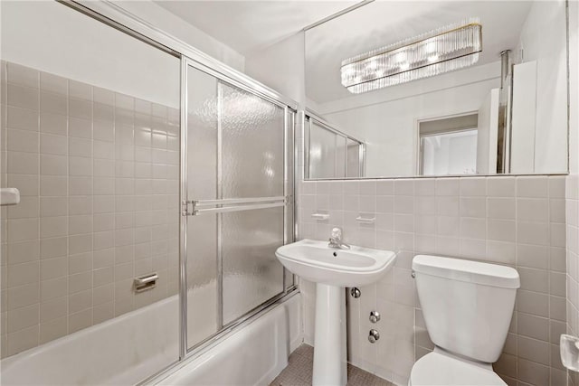 bathroom featuring tile patterned flooring, toilet, tile walls, and bath / shower combo with glass door