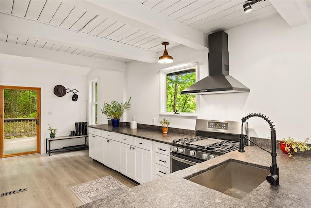 kitchen featuring sink, wall chimney exhaust hood, stainless steel gas range, white cabinets, and light wood-type flooring