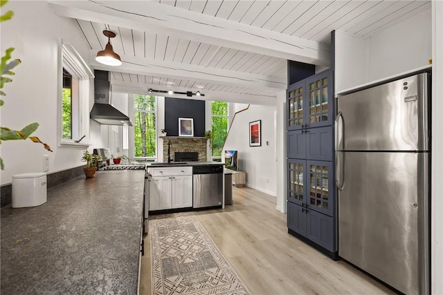 kitchen featuring stainless steel appliances, wall chimney range hood, beam ceiling, light hardwood / wood-style floors, and hanging light fixtures