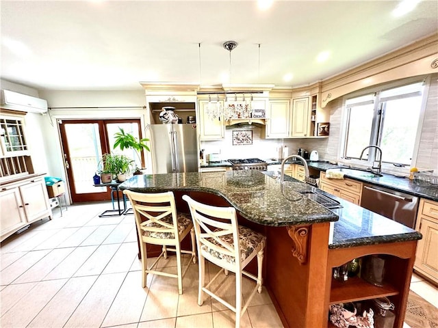 kitchen featuring stainless steel appliances, a wall mounted AC, a kitchen island with sink, sink, and hanging light fixtures