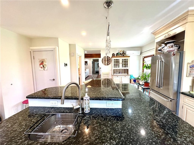 kitchen with high end fridge, dark stone counters, a wall mounted AC, sink, and decorative light fixtures