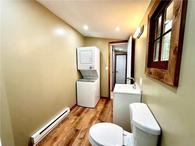 bathroom featuring a baseboard heating unit, vanity, toilet, stacked washing maching and dryer, and hardwood / wood-style flooring