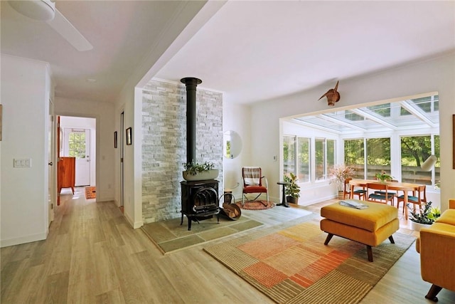 living room with ceiling fan, a wood stove, a wealth of natural light, and light hardwood / wood-style flooring