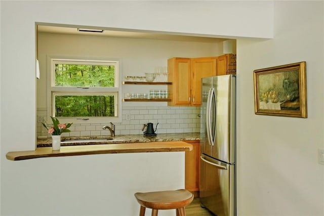 kitchen with stainless steel refrigerator, sink, tasteful backsplash, light stone counters, and a breakfast bar