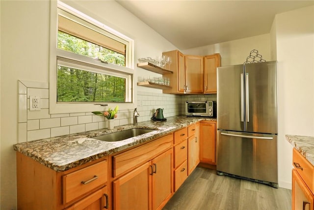 kitchen featuring stainless steel fridge, tasteful backsplash, light stone counters, sink, and light hardwood / wood-style floors