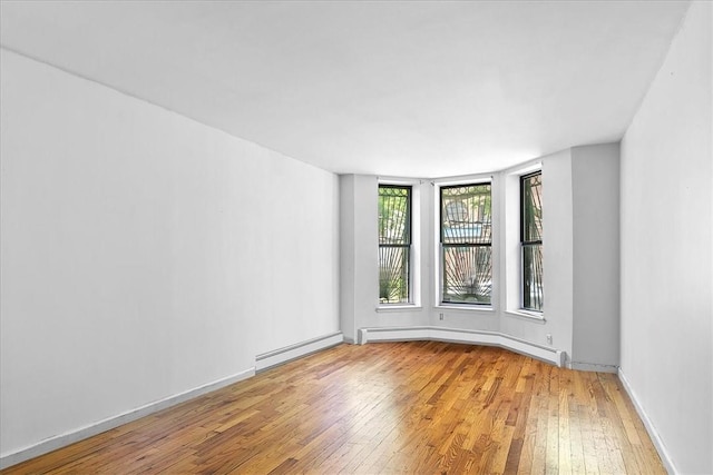 empty room featuring hardwood / wood-style floors and a baseboard heating unit