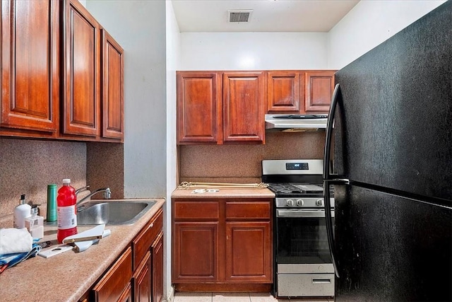 kitchen with gas stove, sink, black fridge, backsplash, and light tile patterned flooring