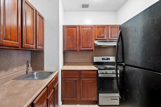 kitchen with gas stove, sink, tasteful backsplash, black refrigerator, and light tile patterned floors