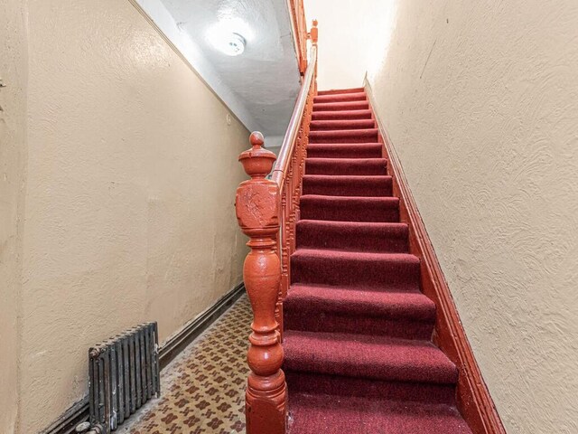 505 E 183rd St, Bronx, NY 10458 - stairway featuring a textured wall, radiator, and baseboards
