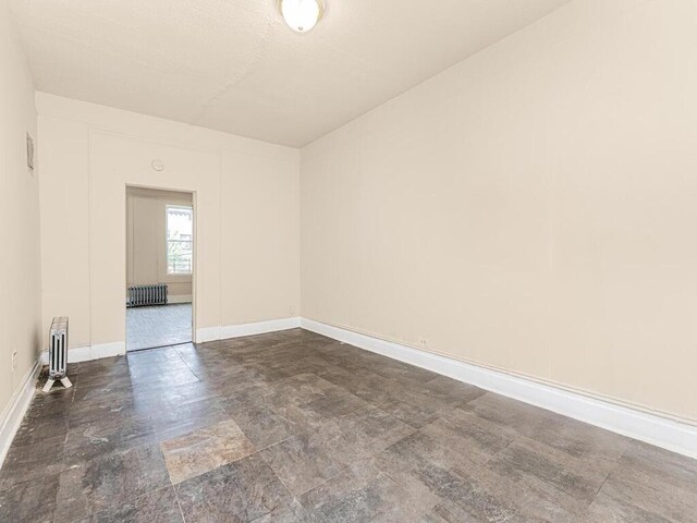 505 E 183rd St, Bronx, NY 10458 - spare room with baseboards, dark stone finish flooring, and radiator