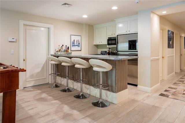 kitchen with white cabinetry, a breakfast bar area, light hardwood / wood-style floors, kitchen peninsula, and stainless steel refrigerator with ice dispenser