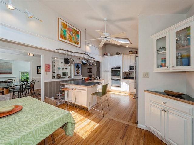 kitchen with white cabinets, vaulted ceiling, light hardwood / wood-style floors, a kitchen island, and a kitchen bar