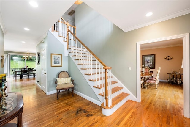 staircase with hardwood / wood-style floors, a notable chandelier, and crown molding