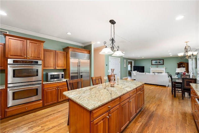 kitchen with pendant lighting, light wood-type flooring, ornamental molding, a kitchen island, and stainless steel appliances