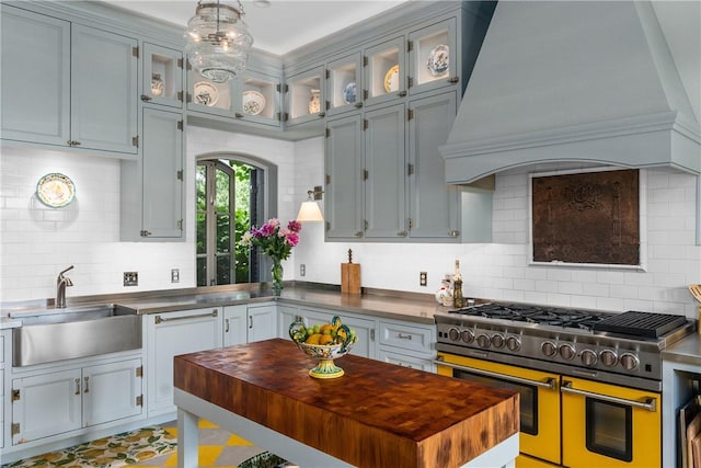 kitchen with backsplash, ornamental molding, custom range hood, sink, and double oven range