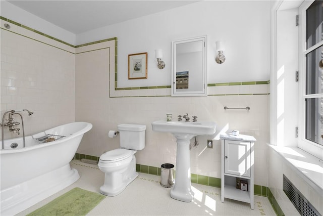 bathroom featuring tile patterned floors, a tub to relax in, toilet, and tile walls