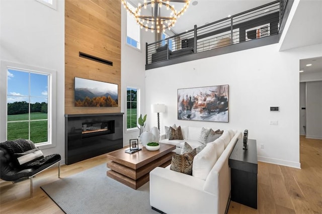 living room featuring a towering ceiling, light hardwood / wood-style floors, an inviting chandelier, and plenty of natural light