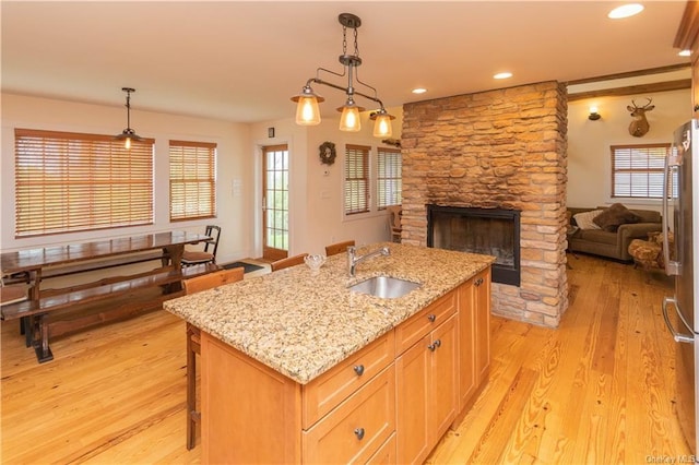 kitchen featuring a kitchen island with sink, sink, hanging light fixtures, light hardwood / wood-style flooring, and light stone countertops