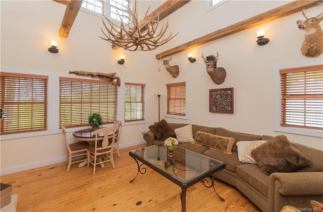 living room featuring a healthy amount of sunlight, light hardwood / wood-style floors, beam ceiling, and a high ceiling