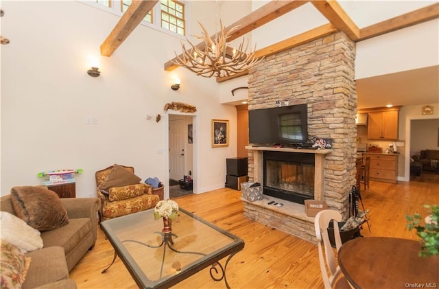 living room featuring a stone fireplace, light hardwood / wood-style flooring, beamed ceiling, and a high ceiling