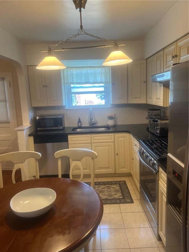 1357 Waring Ave, Bronx, NY 10469 - kitchen featuring appliances with stainless steel finishes, under cabinet range hood, a sink, dark countertops, and light tile patterned floors