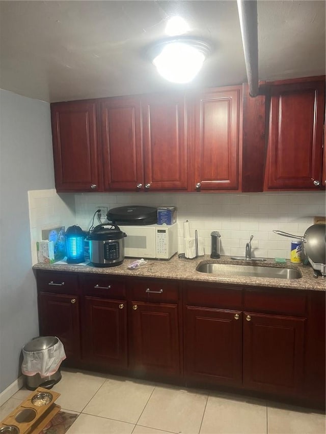 1357 Waring Ave, Bronx, NY 10469 - kitchen featuring reddish brown cabinets, a sink, white microwave, decorative backsplash, and light stone countertops