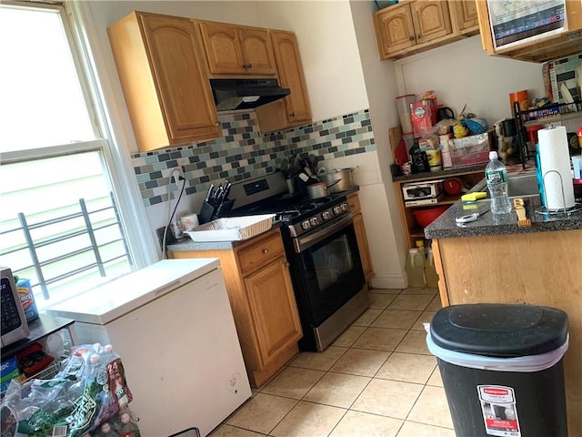 kitchen with backsplash, light tile patterned floors, white refrigerator, stainless steel range with gas stovetop, and range hood