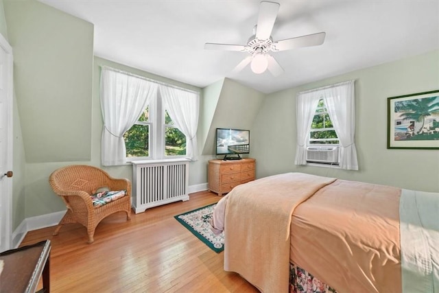 bedroom featuring radiator heating unit, light hardwood / wood-style floors, multiple windows, and ceiling fan