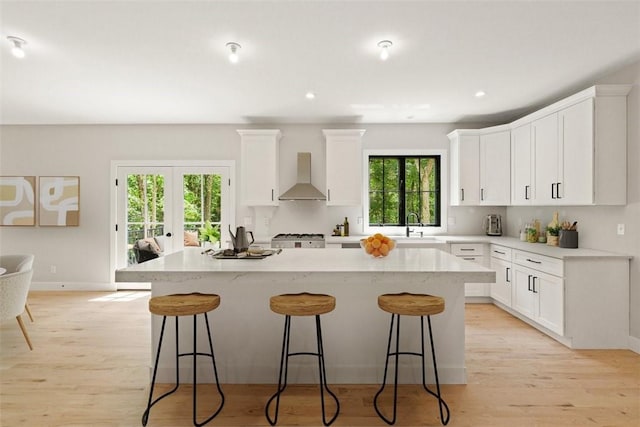 kitchen featuring sink, white cabinets, a center island, range, and wall chimney range hood