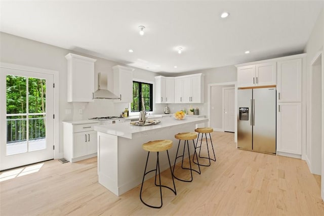 kitchen with tasteful backsplash, white cabinetry, stainless steel refrigerator with ice dispenser, wall chimney range hood, and light hardwood / wood-style flooring