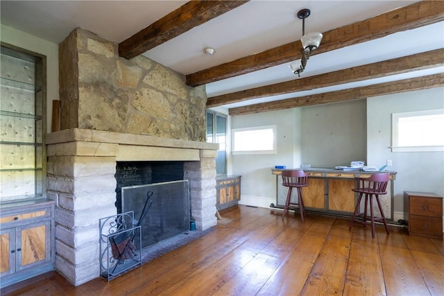 interior space with beam ceiling, a stone fireplace, and hardwood / wood-style floors